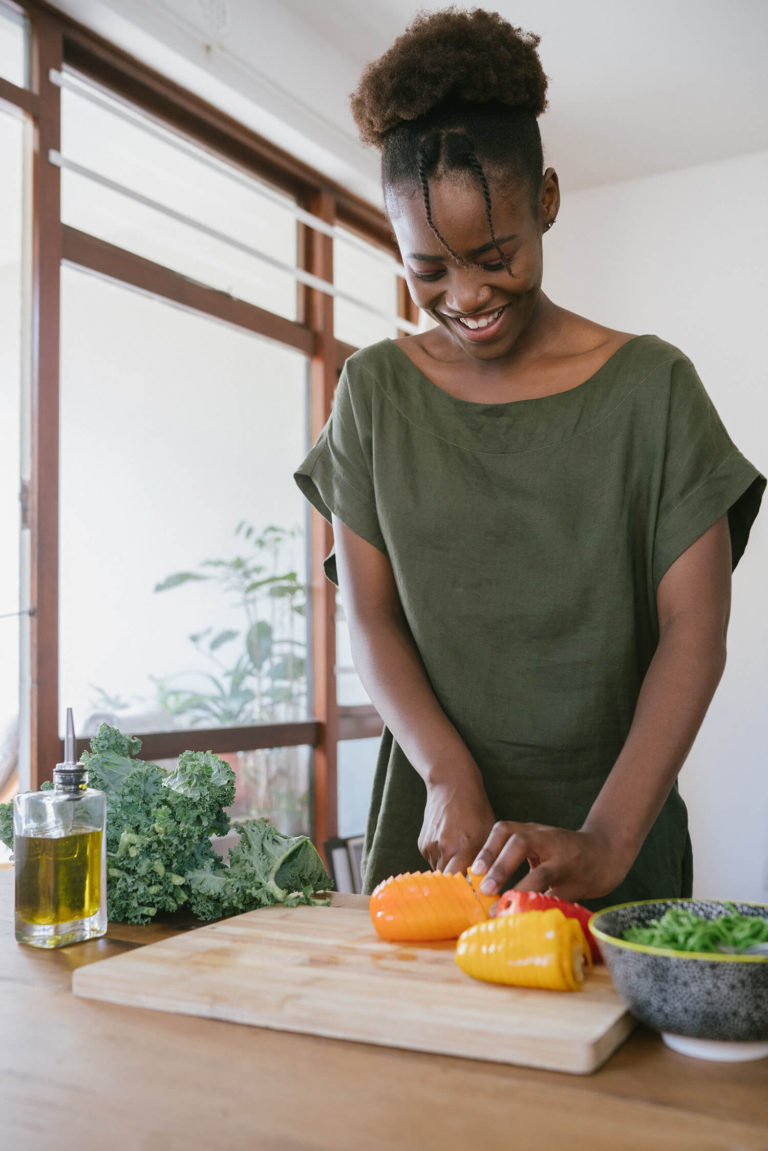 woman in-green tank top cutting orange bell pepper