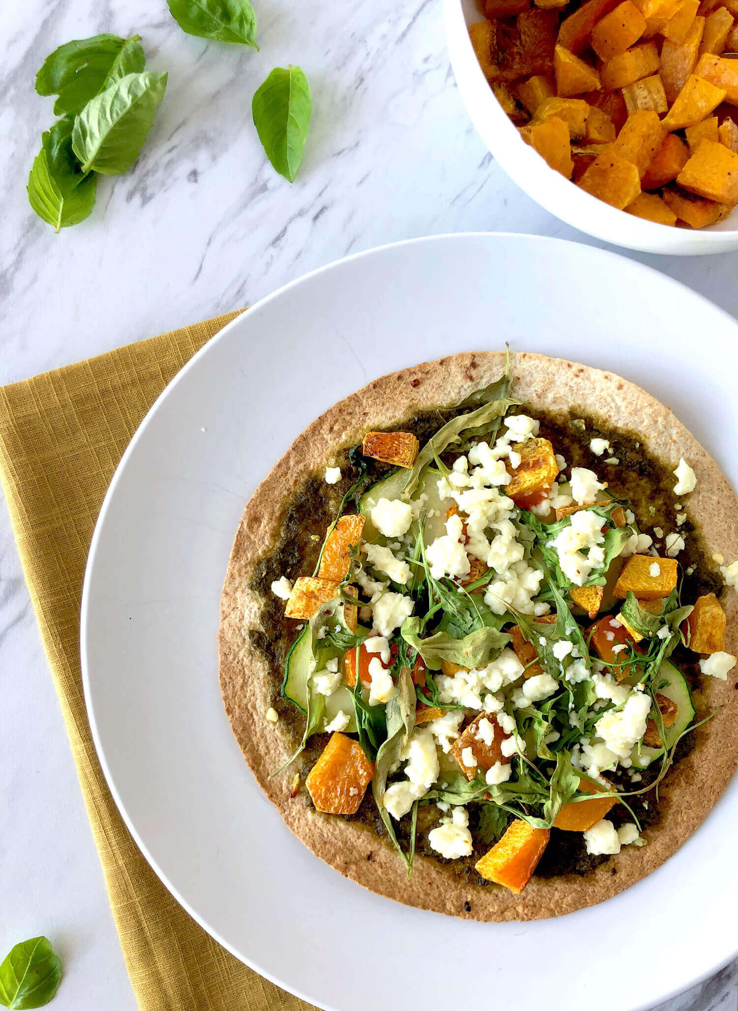 Overhead of a pizza topped with diced squash, arugula, and feta