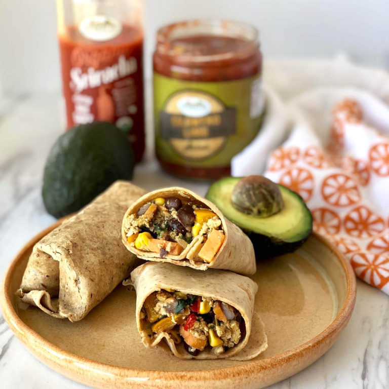 Breakfast burrito sliced in half and served alongside an avocado, salsa, and hot sauce