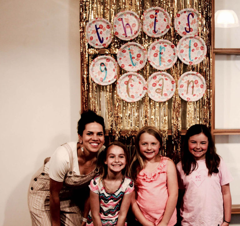 Group of girls all smiling in front of a sparkling banner