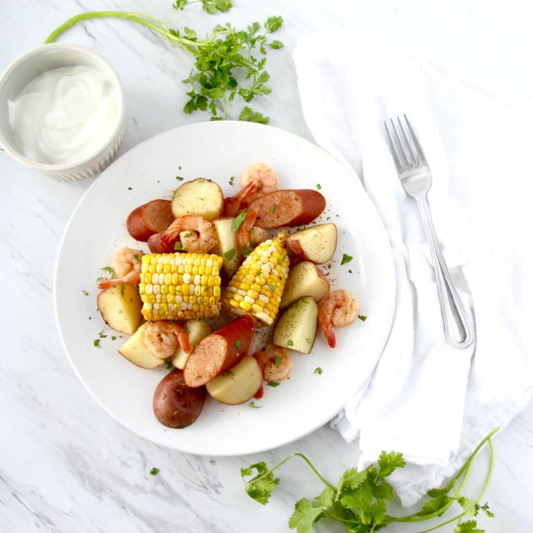 Overhead of shrimp and corn dish sitting next to a fork and condiment